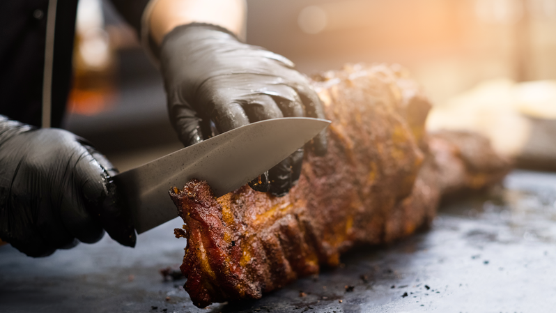 person slicing slab of bbq meat